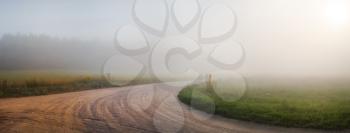 Landscape with an old gravel road in the fog. Turn of gravel road. Panoramic shot. Toned image.