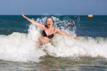 Beautiful young woman in foam and spray of sea wave on a clear sunny day. Shallow depth of field. Focus on model.