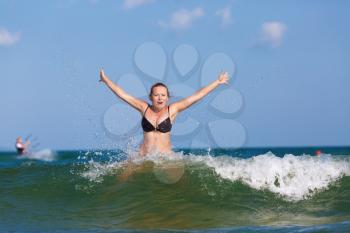 Woman bathing in the sea. Beautiful girl with her hands raised in the foam of a sea wave against the blue sky. Bright sunny day.
