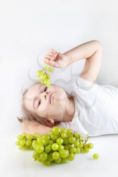 Child, a little girl lying holding a small bunch of grapes and looking into the camera. Bunch of grapes out of focus in the foreground. Vertical shot. Space for text. 