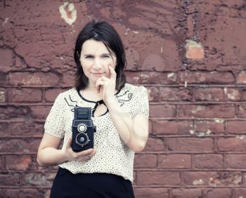 Woman photographer with vintage camera in hand on vintage brick wall background. Toned photo with copy space. Vintage style photo.