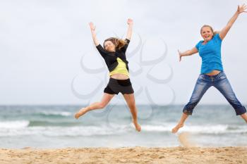 Two happy women jumping on the beach against the sea and cloudless sky. Shallow depth of field. Focus on the models.