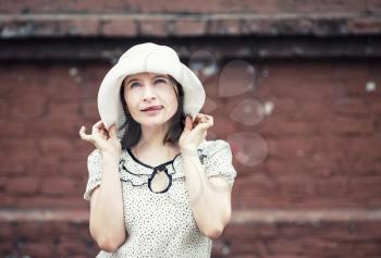 Outdoor lifestyle portrait of pretty young woman in white hat on brick wall background. Girl posing and showing tongue. Vintage style photo. Toned photo with copy space.