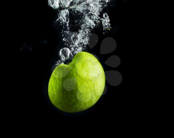 Apple falling into the water with a splash and air bubbles. Fresh green apple in water on black background. Healthy food. Wash fruits.