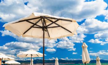 Big white parasols on a background of bright blue sky with cumulus clouds. Beach umbrellas. Shallow depth of field. Selective focus.
