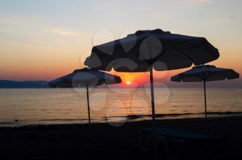 Silhouettes of parasols at dawn. The sun rises over the sea. Shallow depth of field.