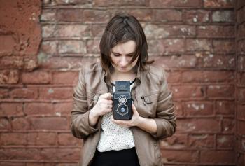 Girl with vintage camera taking photo on brick wall background. Selective focus on camera.