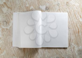 Blank opened book on light wooden background with soft shadows. Template for design presentations and portfolios. Top view.