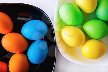 Brightly colored Easter eggs on black and white plates. Easter background. Top view.