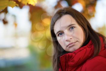 Close-up portrait of a woman in a red jacket on a background of autumn leaves close-up. Bright colorful bokeh. Shallow depth of field. Selective focus. Space for text.