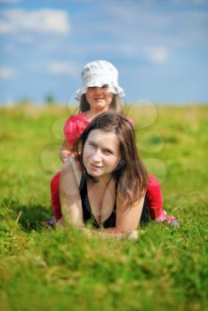 Mom and little daughter in the meadow in the green grass. Sunny summer day. Shallow depth of field. Selective focus on mother's face. Vertical shot.