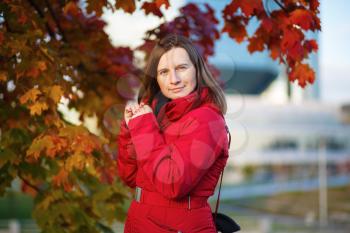 Autumn portrait of a woman. Young woman with long hair in red jacket posing against the backdrop of a maple. Shallow depth of field. Selective focus on model.