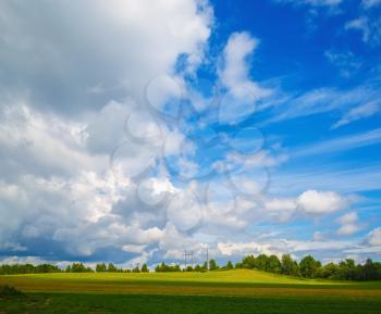 Bright blue sky with cumulus clouds and a field with green grass. Colorful summer landscape.