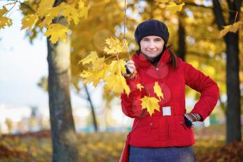 Woman in a beret and red jacket in the autumn park. Girl holding a maple branch with leaves in his hand. Selective focus on model.