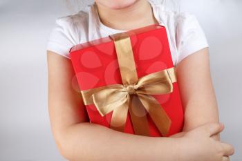 Child holding a red gift box with golden ribbon.