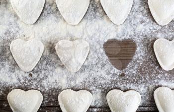 Raw ravioli in the shape of hearts, sprinkle with flour, on wooden background closeup. Cooking dumplings. Top view.