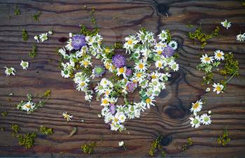 Heart symbol made of wild flowers and leaves on vintage wooden table background. Top view.
