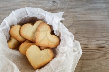 Cookies in the form of hearts in a paper wrapper on a wooden background. Top view.