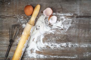 Culinary still life with eggs, eggshells, flour and rolling pin. Vintage cooking background.