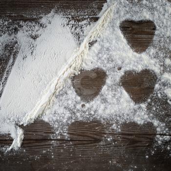 Flour sprinkled on wooden surface, with traces of cookies in the form of hearts. Top view.