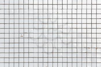 Old white obsolete and damaged tiled wall as a texture or background. White ceramic tile.