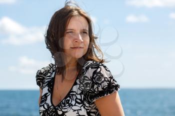 Portrait of woman with wind fluttering hair on blurred background of blue sky and sea.