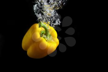 Fresh yellow paprika falling into the water with a splash and air bubbles. Healthy food on black background. Wash vegetables.