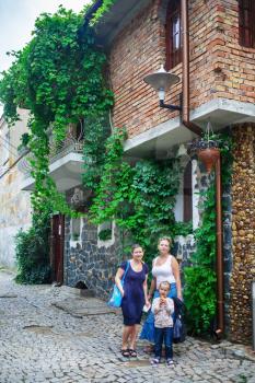 Two young women and a little girl on a background of an ancient building overgrown with ivy. Family portrait outdoors. Women in the old town. Vertical shot.