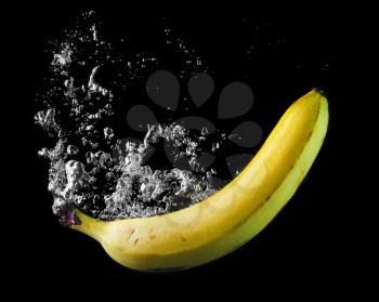 Ripe banana dropped into the water with a splash and air bubbles. Healthy food on black background. Wash fruits.