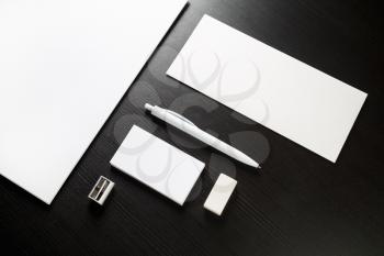 Photo of blank stationery on black wood table background. Envelope, business cards, pen, letterhead, sharpener and A4 paper. Top view.