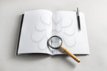 Photo of blank opened book, magnifier and pencil on paper background. Stationery elements. Template for placing your design. Responsive design mockup.