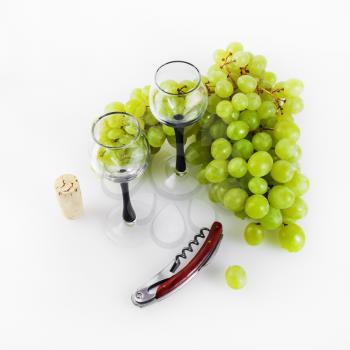 Green grapes, glass goblets, corkscrew and cork on a light background. Still life with grapes.