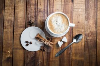 Delicious fresh coffee. Coffee cup with cinnamon sticks, coffee beans, anise, sugar, spoon and coasters on vintage wooden kitchen table background. Top view.