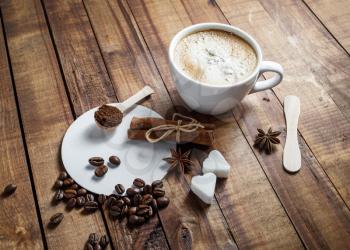 Coffee cup with cinnamon sticks, coffee beans, anise, sugar, spoon and coasters on vintage wooden background. Still life with coffee.