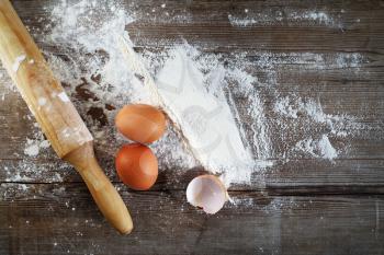 Eggs, flour and rolling pin on vintage wooden table background. Top view.
