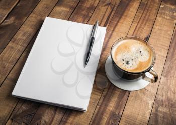 Photo of blank closed book, pencil and coffee cup on wooden table background. Responsive design mockup. Stationery elements. Template for placing your design.