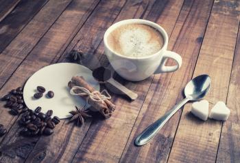 Still life with coffee. Photo of coffee cup, cinnamon sticks, coffee beans, anise, sugar, spoon and coasters on vintage wood background.