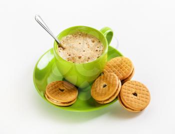 Green cup of coffee and cookies on white paper background.