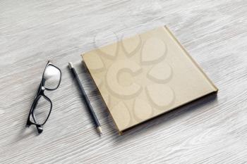 Blank square notebook or book, glasses and pencil on light wood table background. Template for branding design.