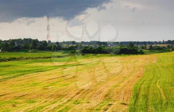 Scenic rural landscape. Field after haymaking, grass, trees and bushes, cloudy sky
