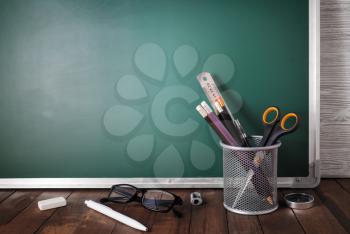 Photo of school stationery on blank green chalkboard background. Copy space for text.