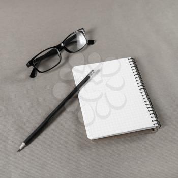 Blank notebook, glasses and pencil on craft paper background.