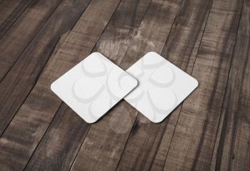 Photo of two blank white square beer coasters vintage wood table background.