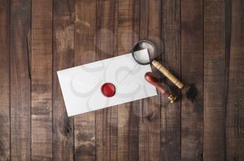 Blank paper envelope with wax seal, stamp and magnifier on wood table background. Mockup for your design. Flat lay.