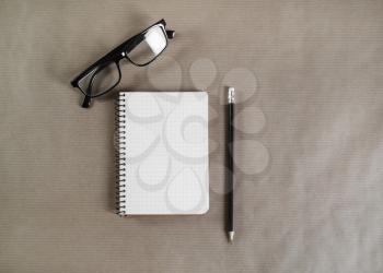 Blank notepad, glasses and pencil on craft paper background. Flat lay.