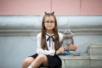 Child girl with plush toy and textbooks sits on the steps of the school stairs. Schoolgirl portrait. Selective focus.