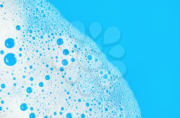 Foam with bubbles on blue background. Soap sud. Detergent in water. Abstract soapy texture. Flat lay.