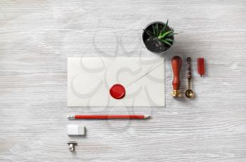 Vintage blank envelope with wax seal, stamp, pencil, eraser, plant, spoon and postcard on light wooden background. Top view. Flat lay.