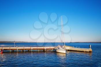 Yacht at the pier. Blue cloudless sky and reflection in water. Space for text.