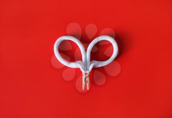 White bracelets clamped in a clothespin on red backgroung. Two bracelets in the form of scissors or a heart. Flat lay.